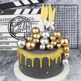 gold and silver faux balls used on a black cake with gold drip and a gold feather topper
